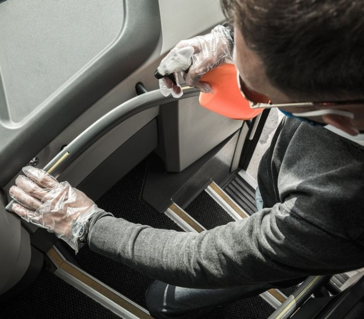 Charter bus driver sanitizing a charter bus handrail