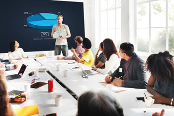 business people sit at a table and watch a presentation