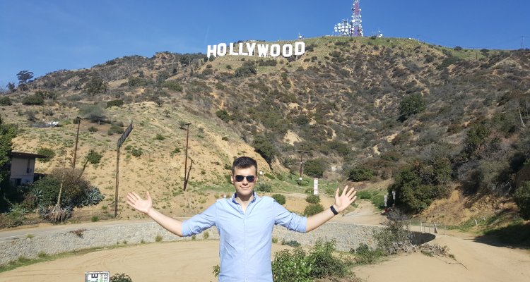 a man stands with his arms open in front of the hollywood sign