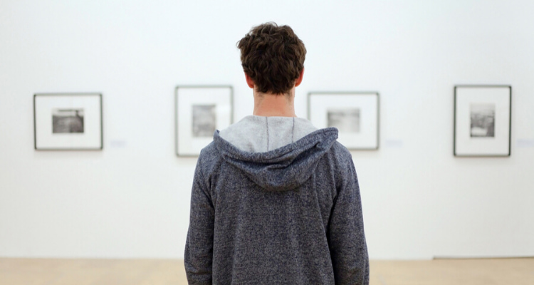 a man looks at pieces of photography on a blank white wall