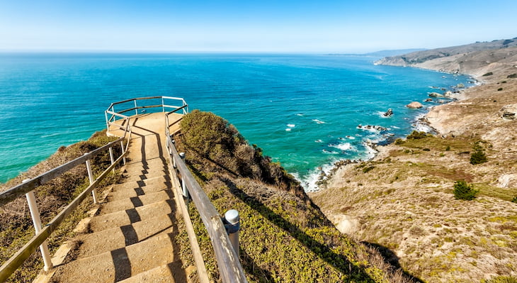 View from the lookout point over Muir Beach in California. A railed-off outcropping fills the foreground while the rocky Pacific coast lies in the background